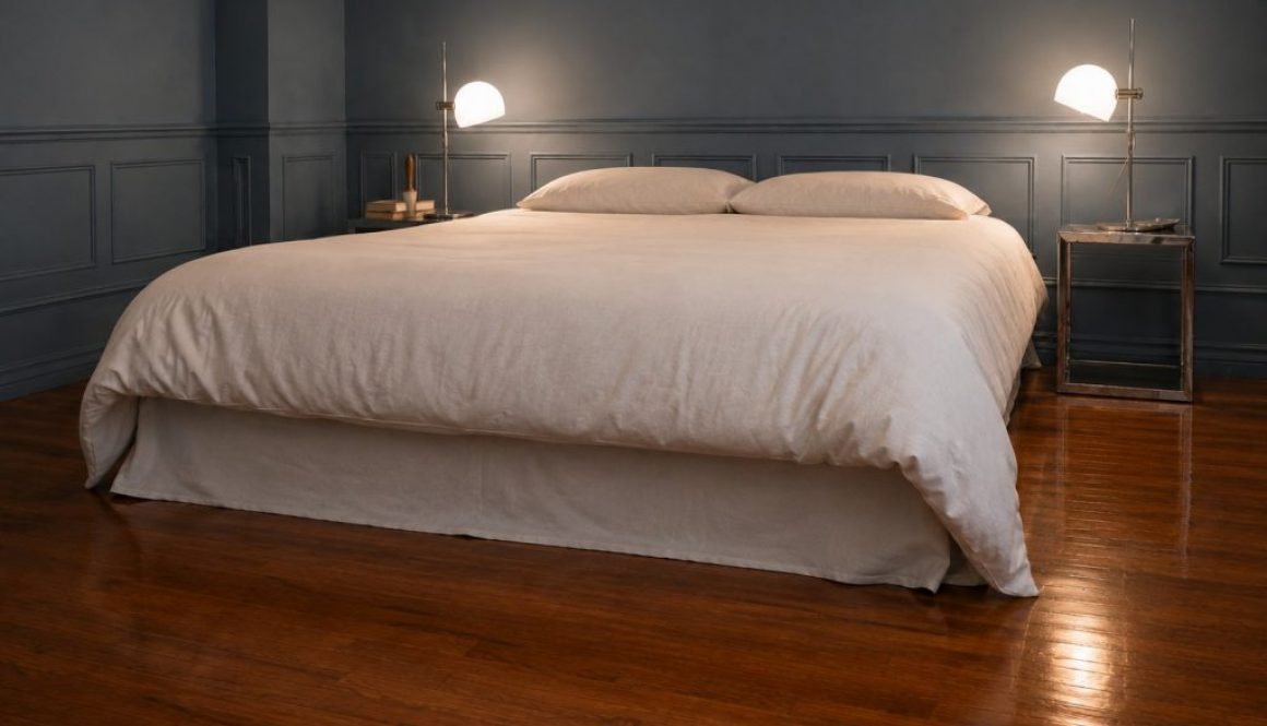 Finished bed with a white duvet and a no-sew flat-sheet bed skirt in a blue-grey bedroom with matching wainscoting and bedside lamps.
