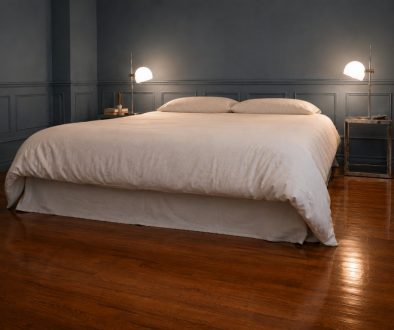 Finished bed with a white duvet and a no-sew flat-sheet bed skirt in a blue-grey bedroom with matching wainscoting and bedside lamps.