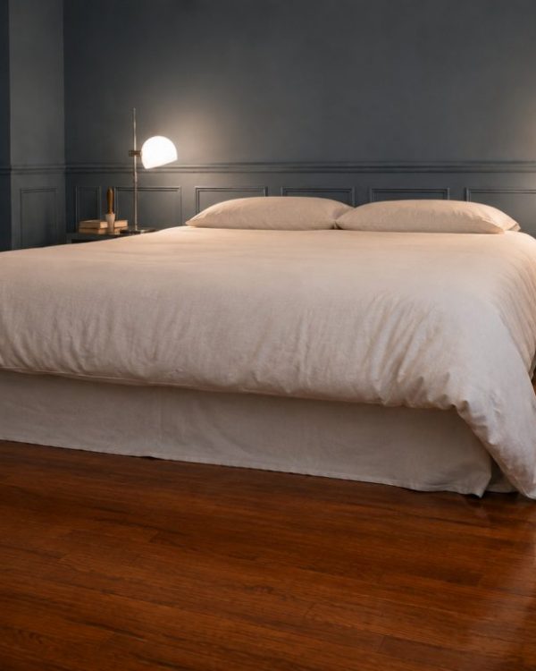 Finished bed with a white duvet and a no-sew flat-sheet bed skirt in a blue-grey bedroom with matching wainscoting and bedside lamps.