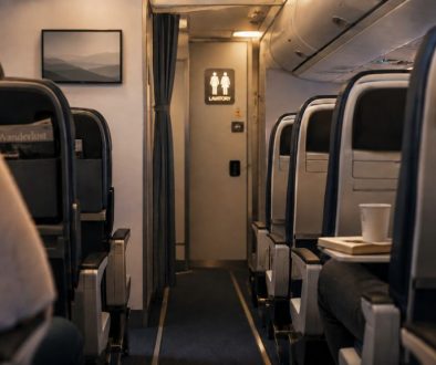 Softly lit airplane aisle with rows of seats and a lavatory sign visible at the back of the cabin.